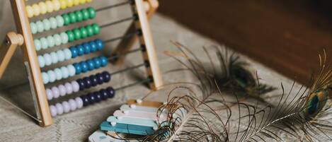 A wooden abacus with colorful beads, a feather, and a book on a textured surface.