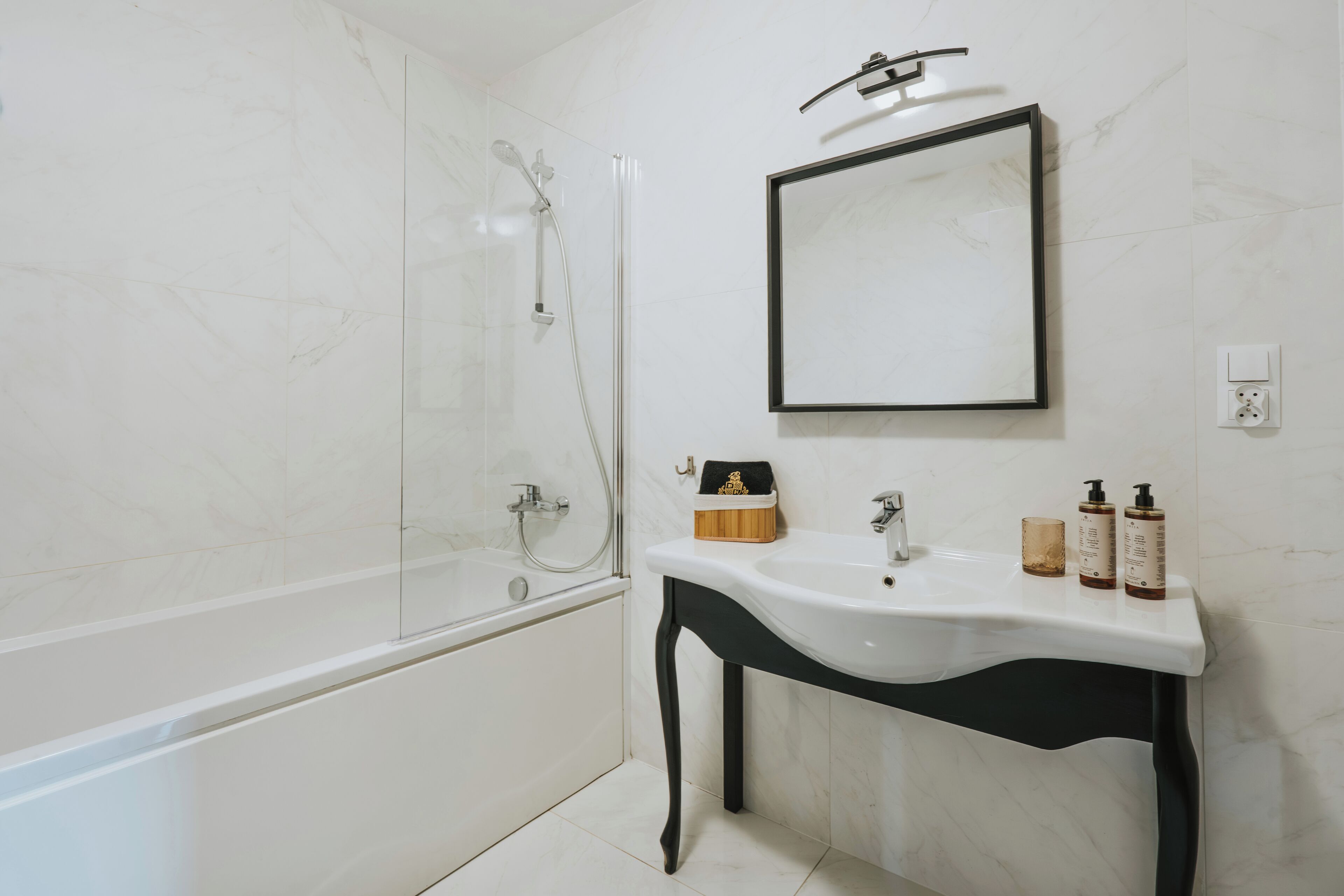 Un baño moderno con ducha envuelta en vidrio, un lavamanos blanco con patas negras y un espejo sobre el lavamanos.