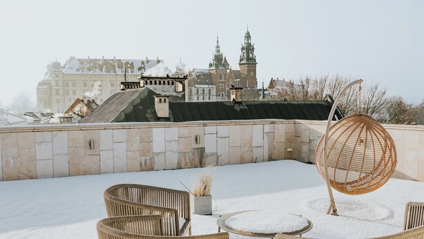 A rooftop terrace with wicker furniture and a spherical hanging chair, overlooking a historic building with a clock tower. - Bogoria House (Kraków)