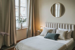 A neatly made bed with a headboard, a bedside lamp, and a window with curtains.