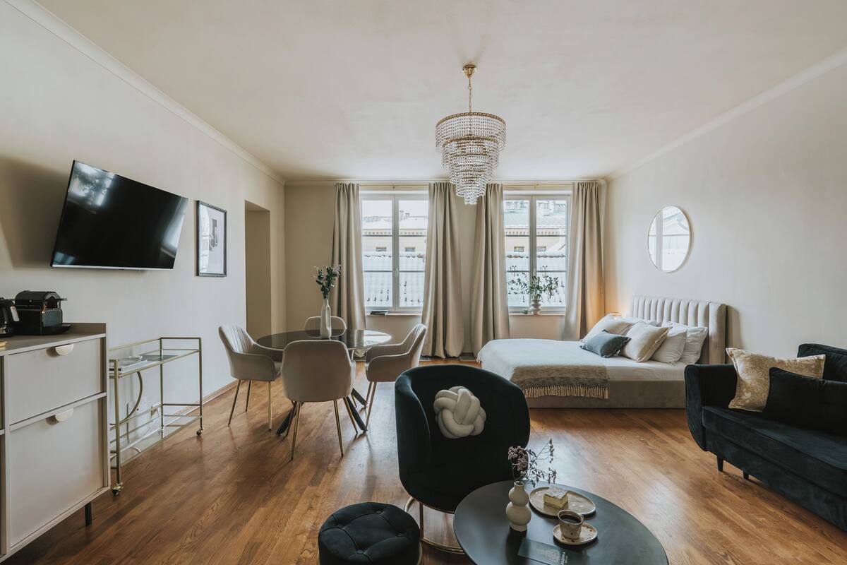 Een moderne woonkamer met een bank, een eethoek, een aan de muur bevestigde televisie en een kroonluchter.