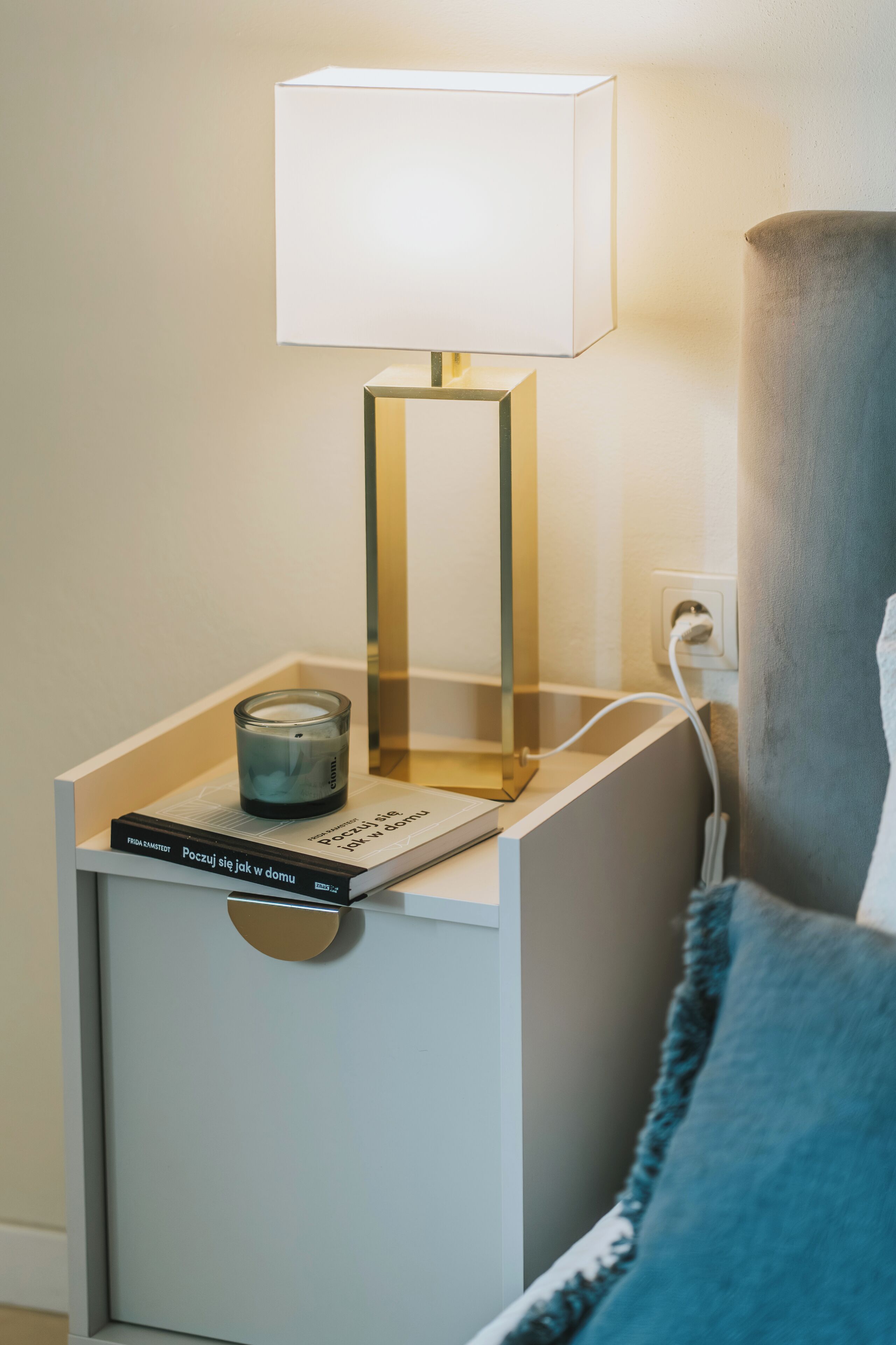A bedside table with a lamp, a book, and a candle.