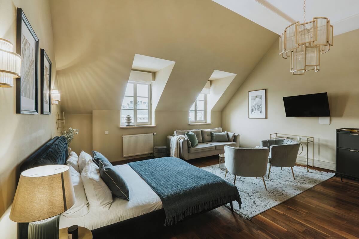 Ruime slaapkamer met een groot bed, een zithoek met een bank en stoelen, een flatscreen televisie en een kroonluchter.
