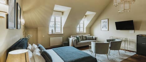 Une chambre spacieuse avec un grand lit, un coin salon avec un canapé et des fauteuils, un téléviseur à écran plat et un lustre.