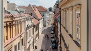 A street view through a window with buildings on either side, a cobblestone street, and parked cars. - Bogoria House (Kraków)