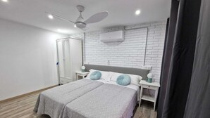 Une chambre à coucher avec un lit, des tables de chevet, un ventilateur de plafond et un mur en briques blanches.