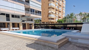 Une piscine dotée d’une terrasse carrelée, entourée d’un immeuble à plusieurs étages avec des balcons.