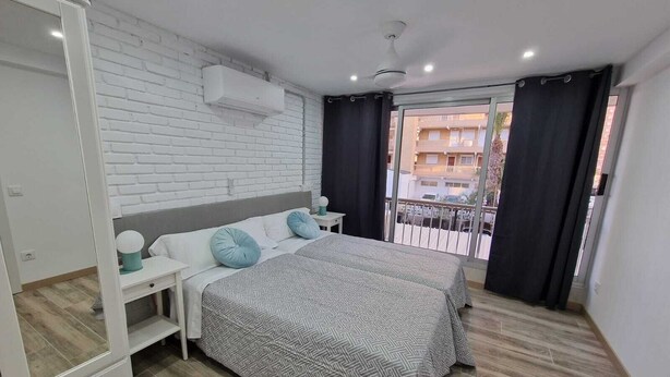 Une chambre à coucher comprenant un lit, une armoire, une table de chevet, un ventilateur de plafond et une fenêtre avec des rideaux.
