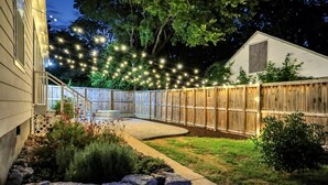A backyard with a wooden fence, a stone wall, and string lights. - Luxury Memphis Musical Estate! Pool, Games! (Memphis)
