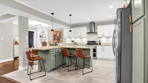 A modern kitchen with a central island, bar stools, and a stainless steel refrigerator. - Luxury Memphis Musical Estate! Pool, Games! (Memphis)