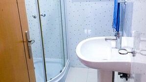 Une salle de bain avec une douche à parois de verre, un lavabo blanc et une serviette bleue posée sur un porte-serviettes.