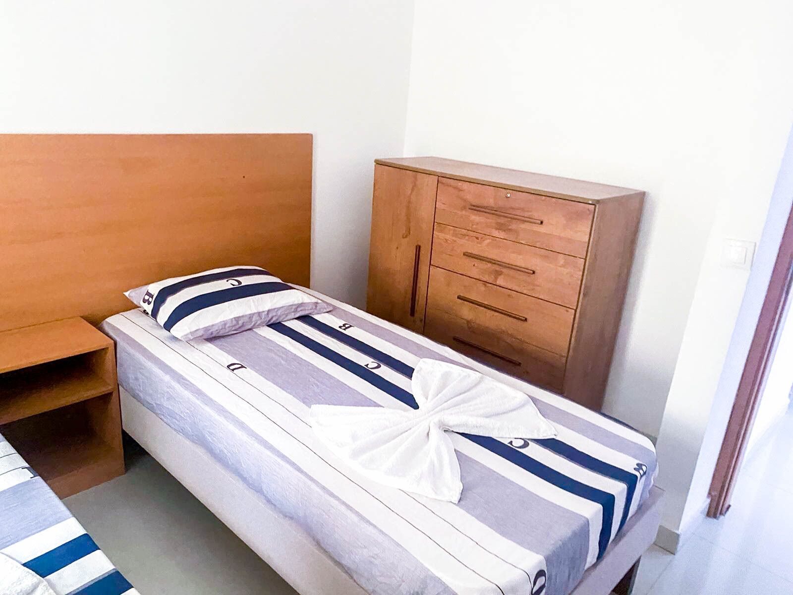Una cama individual con ropa de cama a rayas, un cabecero de madera y un aparador de madera con cajones.
