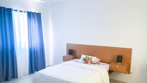 Une chambre d’hôtel avec un grand lit, deux tables de chevet, une tête de lit en bois et une fenêtre avec des rideaux bleus.