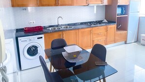 Une cuisine compacte avec des meubles en bois, un lave-linge encastré et une table à manger en verre, accompagnée de chaises.