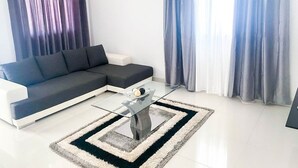 Un salon moderne avec un canapé d’angle, une table basse en verre et un tapis à motifs.