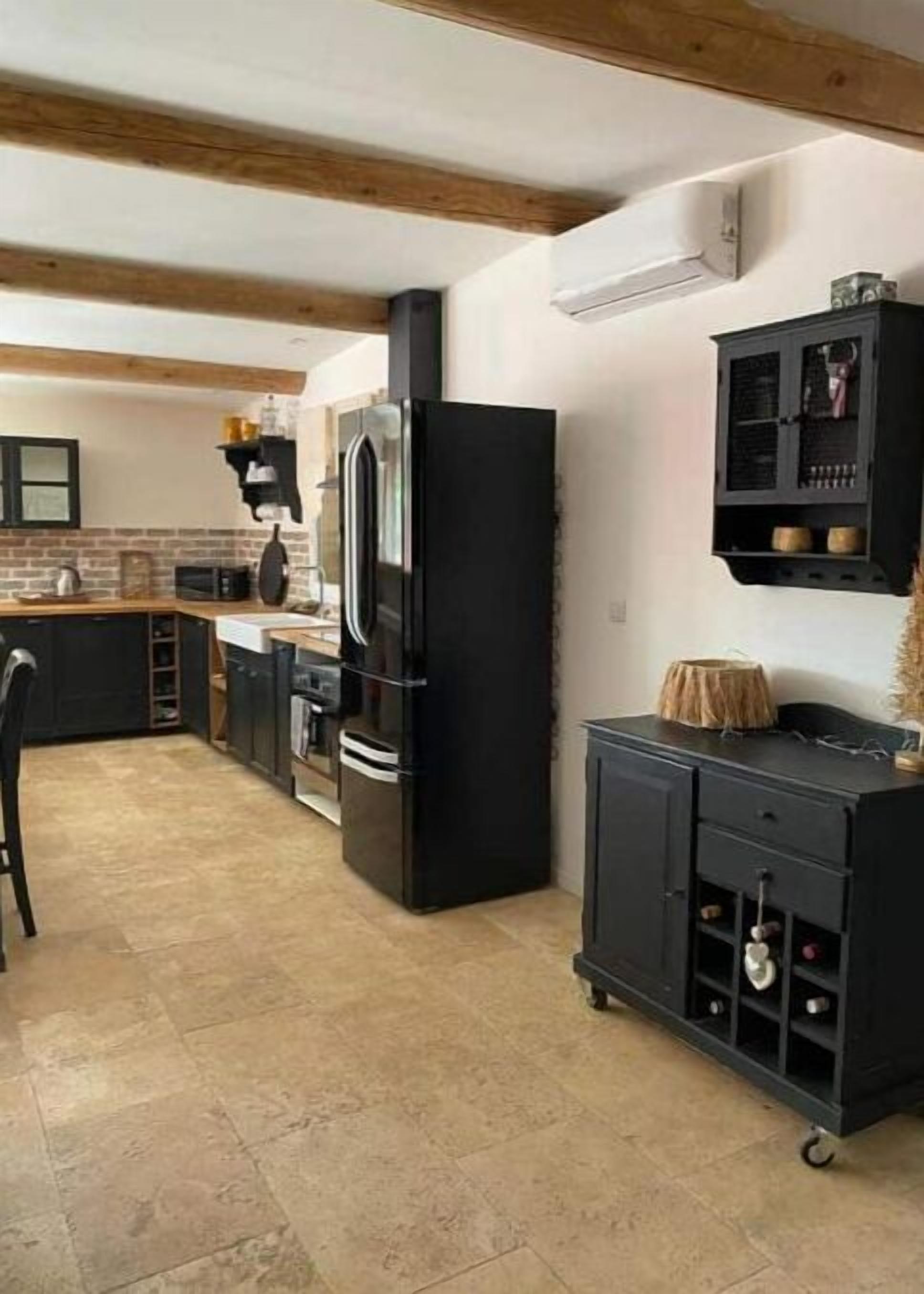 Une cuisine avec un réfrigérateur noir, un four à micro-ondes et une cuisinière. Le plafond est en bois et il y a un meuble noir avec un porte-bouteilles.