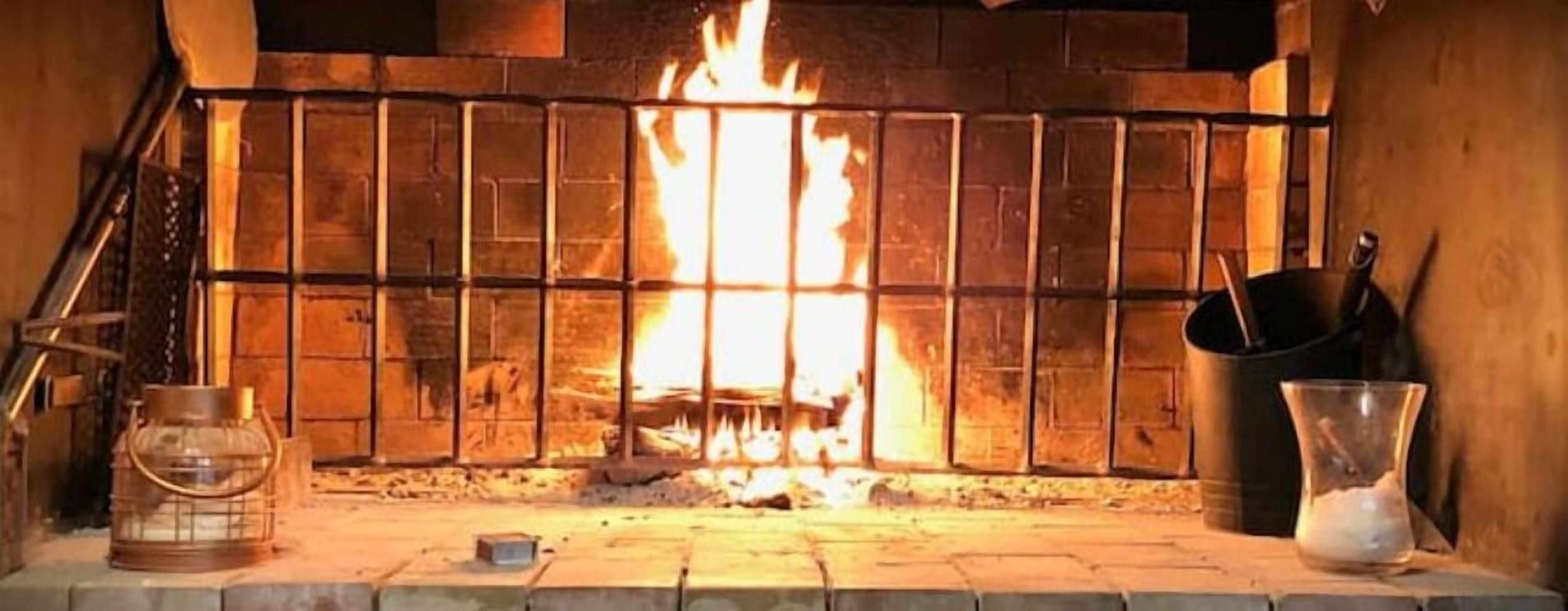 Una chimenea con fuego encendido, un farol y una olla sobre la repisa.