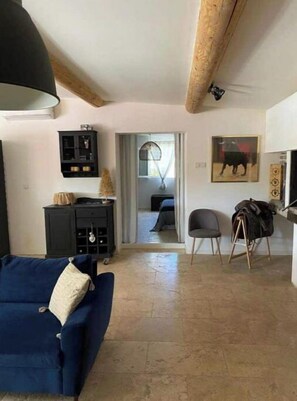 A living room with a blue sofa, a black cabinet, and a dining area with a chair and a coat rack.