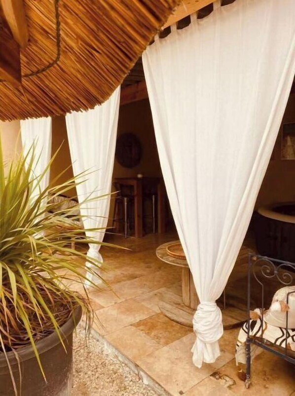 A covered outdoor area with a potted plant, white curtains, and a metal railing.