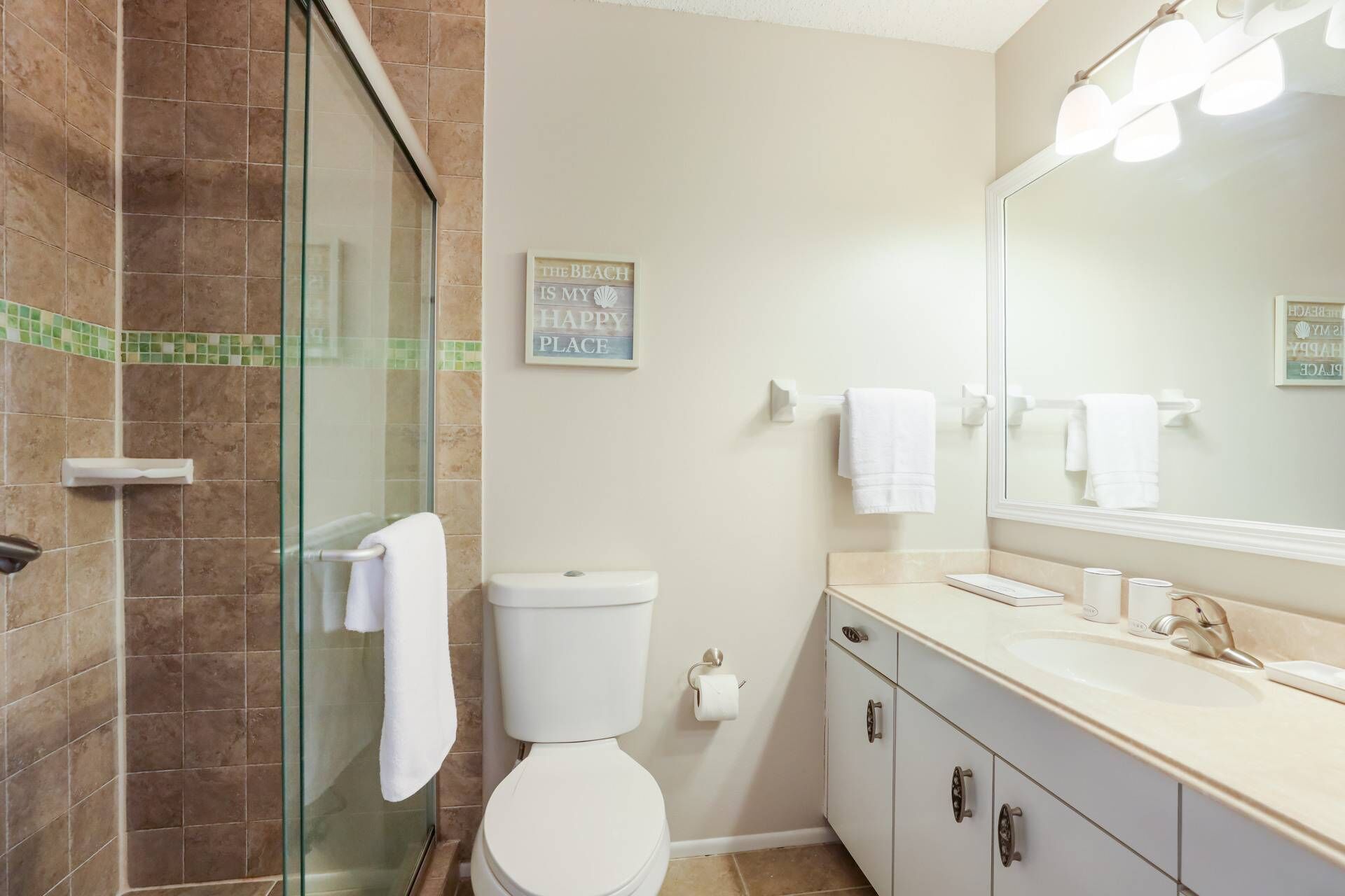 A bathroom with a glass shower enclosure, a toilet, a sink with a mirror, and a towel rack.