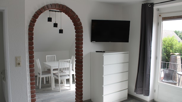 Una habitación con un arco de ladrillo, un aparador blanco, un televisor de pantalla plana y un comedor con sillas blancas.