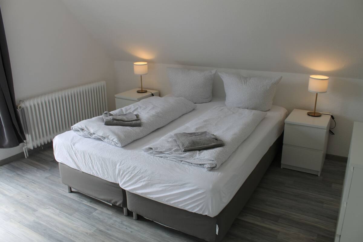A modern bedroom with a large bed, two bedside tables, and a radiator.