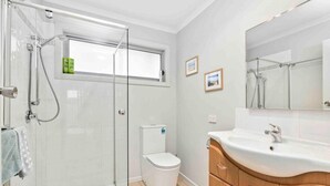 Ein Badezimmer mit Duschkabine aus Glas, Toilette, Waschbecken mit Spiegel und Holzschränken.
