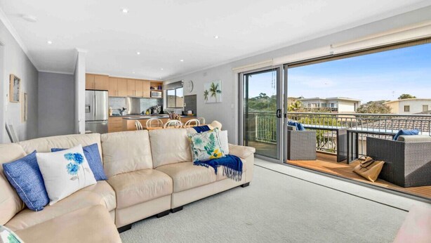 Ein modernes Wohnzimmer mit einem beigefarbenen Sofa, einem Essbereich und einem Balkon mit Korbmöbeln.
