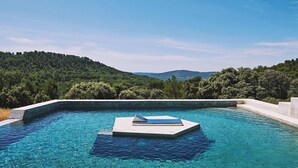 Ein Schwimmbecken mit einer schwimmenden Liegeinsel, umgeben von üppiger Vegetation und Hügeln im Hintergrund.