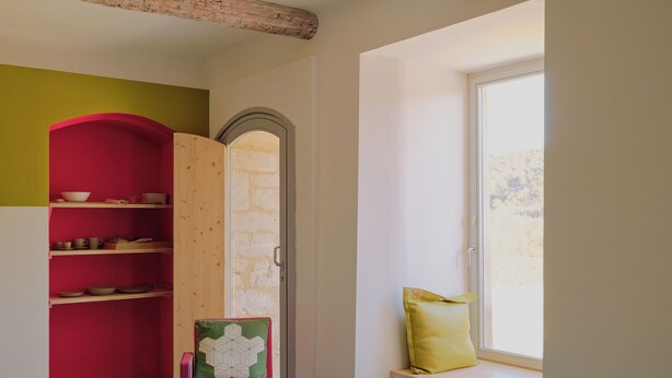 Ein Zimmer mit einem Holzstuhl, einer Fensterbank mit Kissen und einer Regalvorrichtung in Rot und Grün.