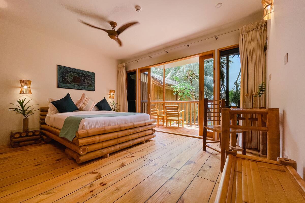 Una habitación con cama, suelo de madera, ventilador de techo y vistas al exterior.