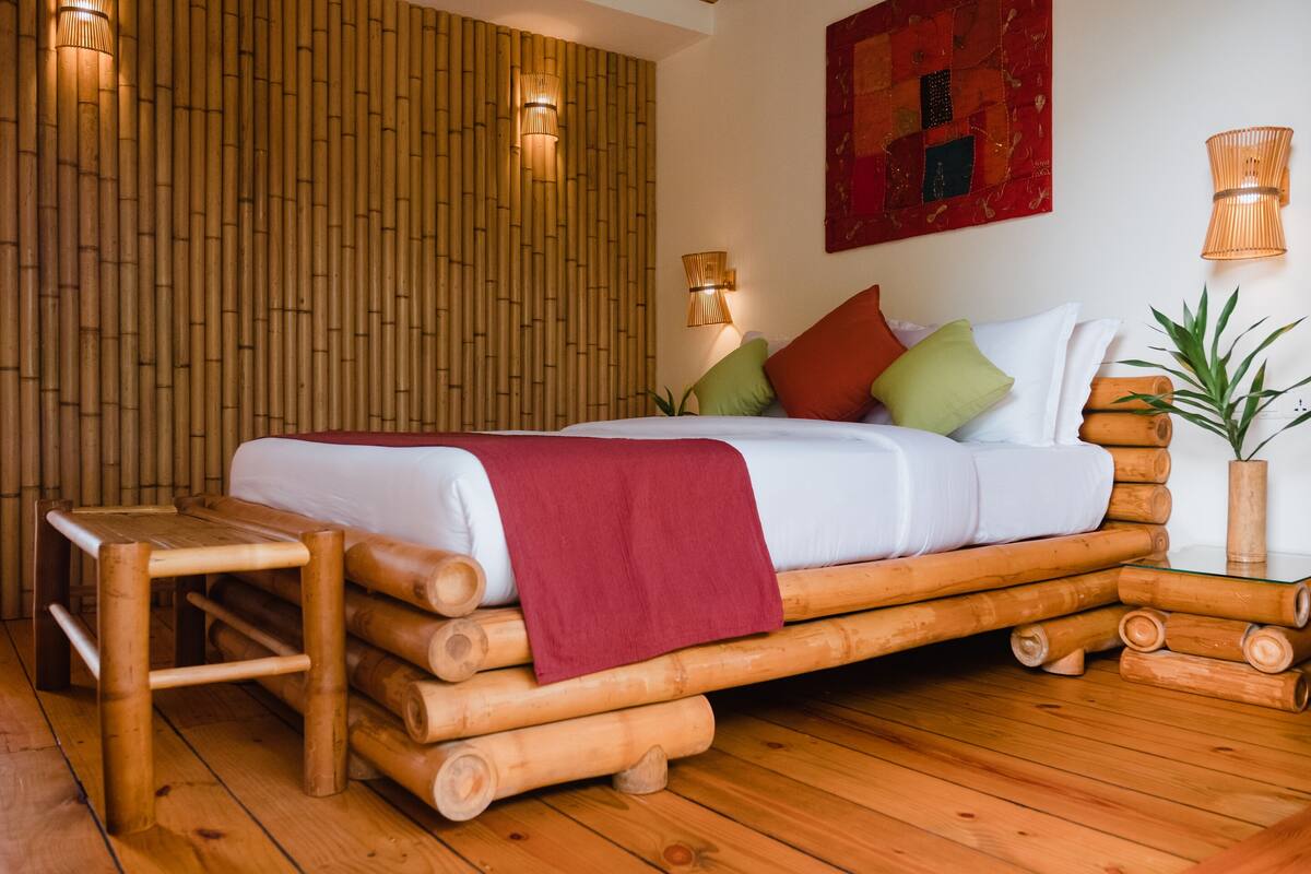 Una habitación con una cama hecha de troncos, un banco de madera y una pared con paneles verticales de bambú.