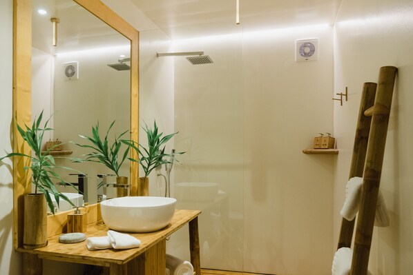 A modern bathroom with a wooden vanity, a large mirror, and two potted plants.