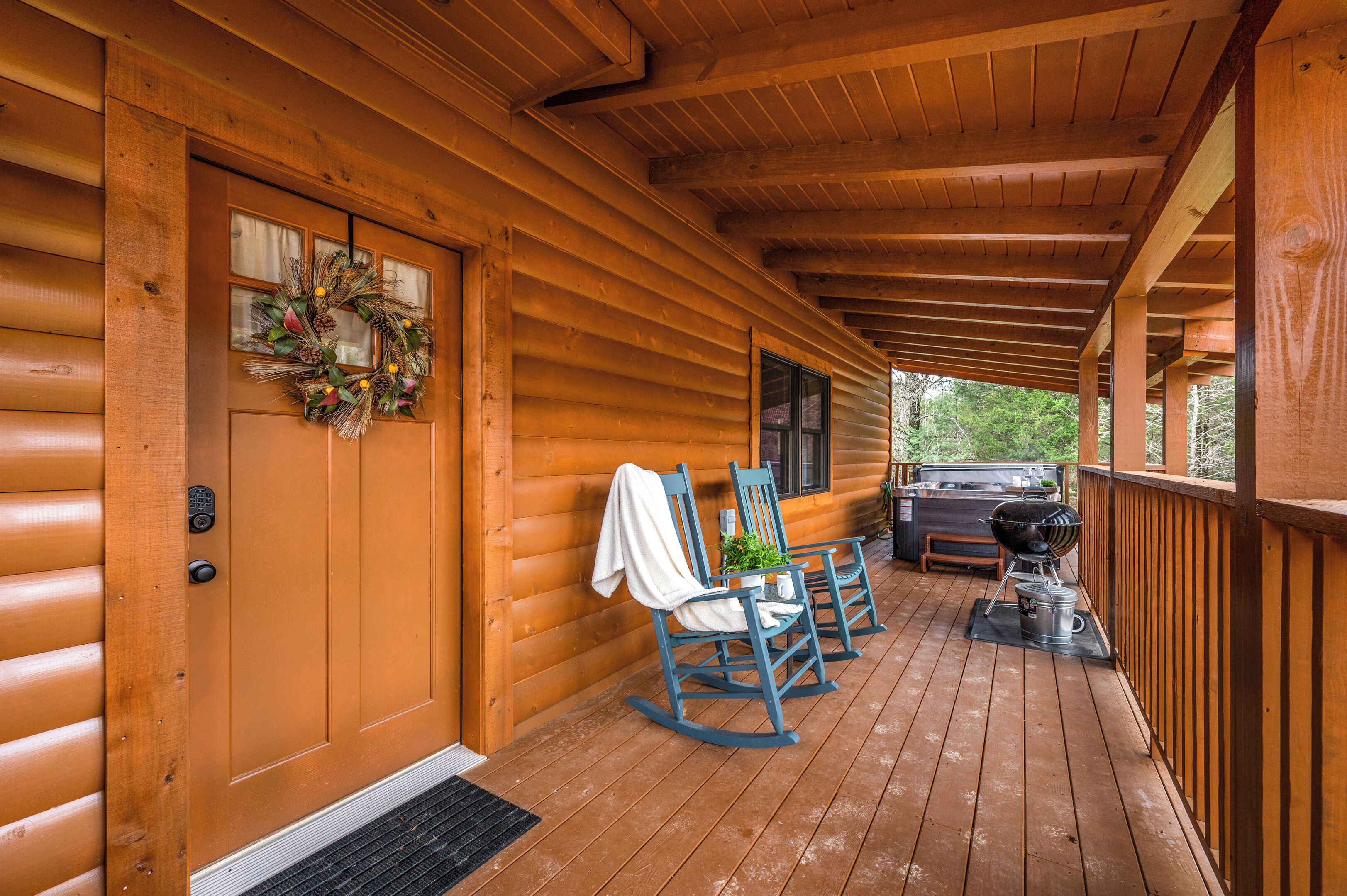 Eine Holzhütte mit Veranda, einer Tür mit einem Kranz, Schaukelstühlen und einem Grill.