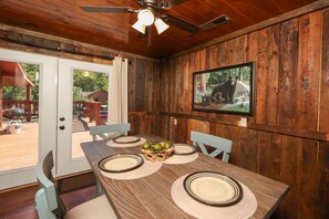 A dining area with a wooden table set for four, a ceiling fan, and a television mounted on the wall.