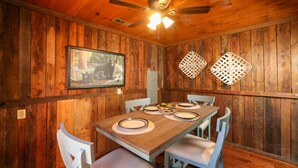 A wooden dining room with a table set for four, white chairs, and a ceiling fan. - Newly Remodeled Private Cabin - Hot Tub, Firepit, Video Arcade Game (Sevierville)