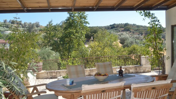 Une terrasse extérieure avec une table ronde, des chaises et un saladier rempli de fruits.