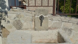 Un mur de pierre avec une porte en métal et un puits en pierre.