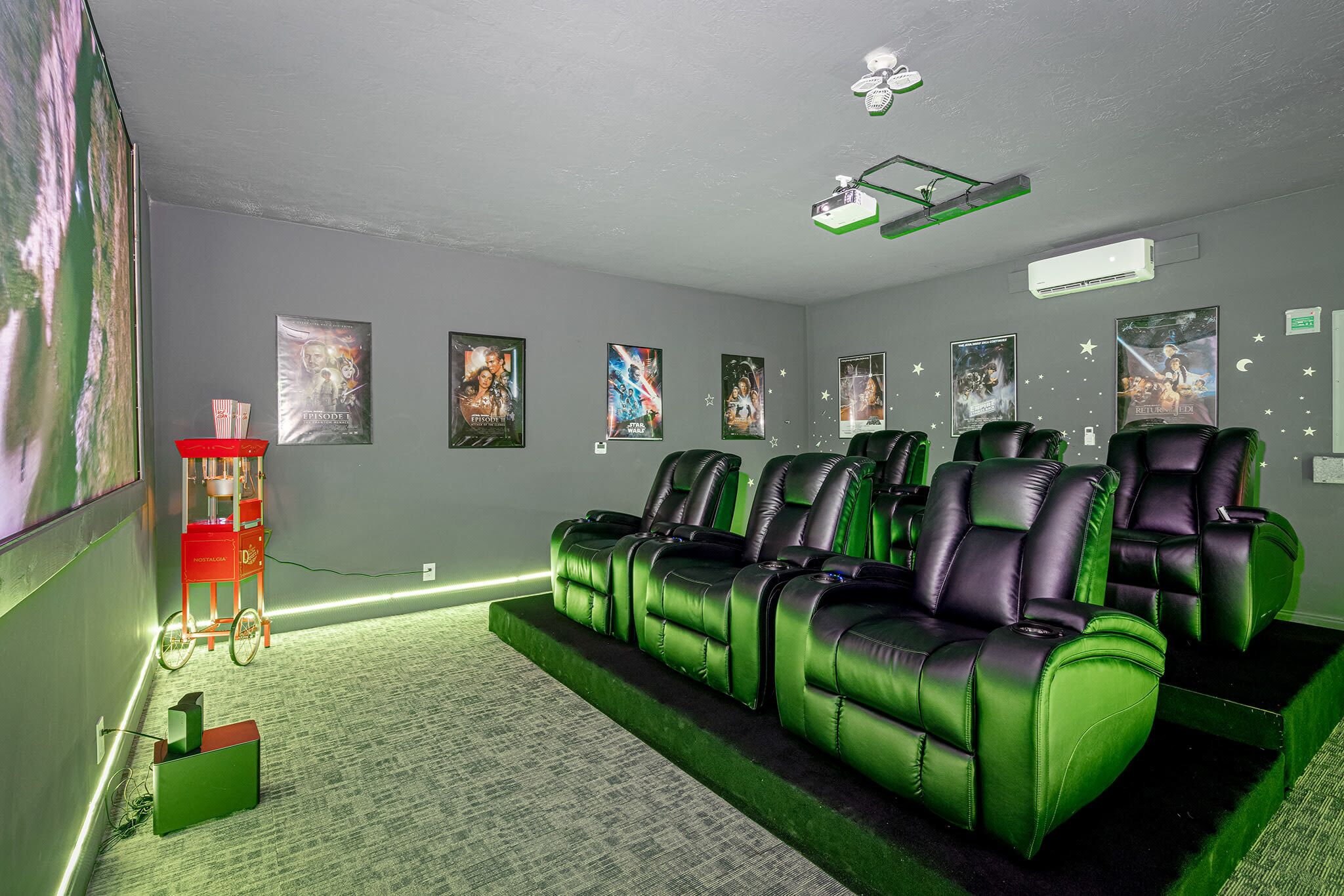 Une salle de cinéma privée avec des fauteuils inclinables en cuir vert, un appareil à pop-corn rouge et des affiches de films accrochées au mur.
