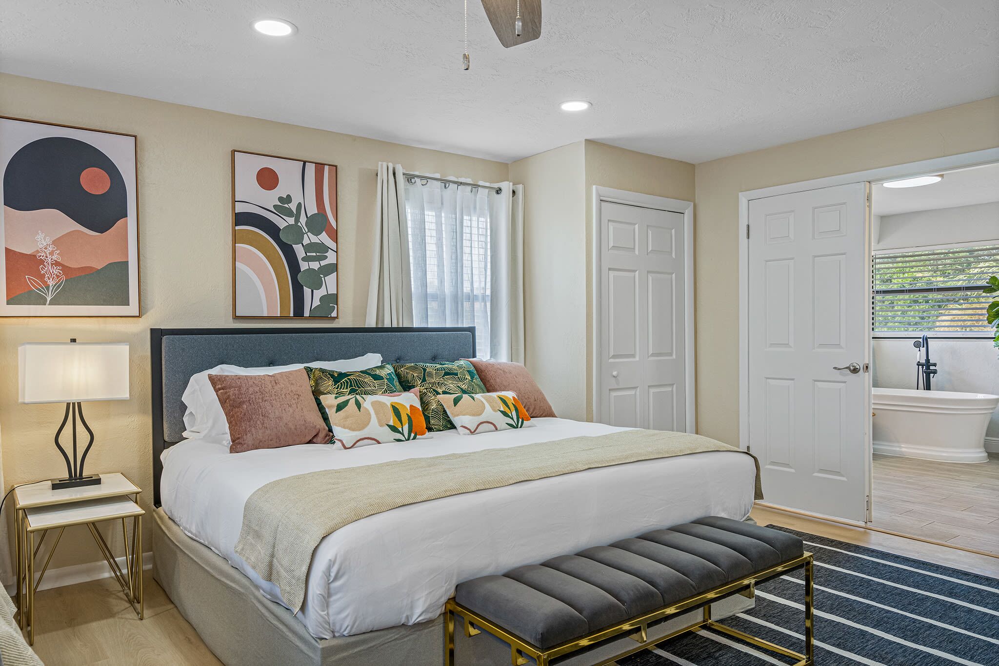 A bedroom with a bed, bedside table, bench, and artwork on the wall.