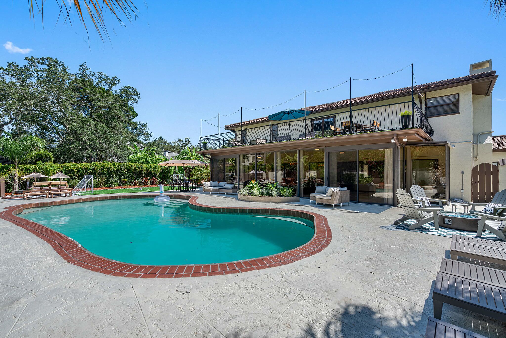 A swimming pool with a brick border, outdoor seating, and a covered patio area.