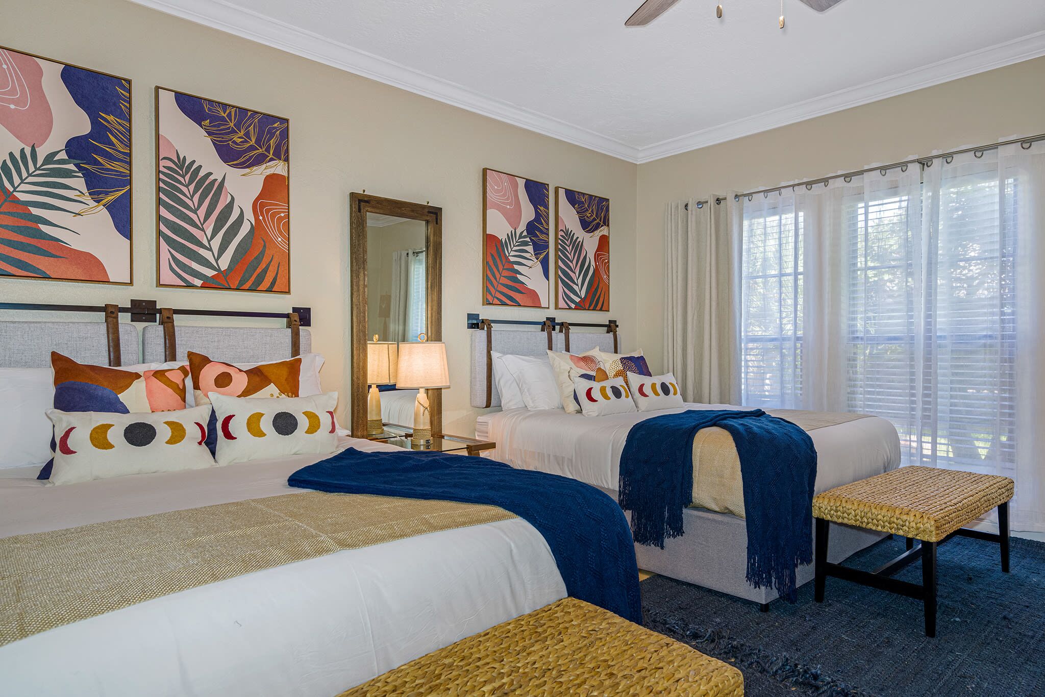A hotel room with two beds, a bench, a mirror, and artwork on the walls.
