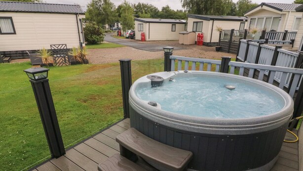 Un jacuzzi en una terraza de madera con escalones que llevan a él, rodeado por una barandilla y un pequeño jardín.