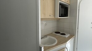 Pieni, käytännöllinen keittiö, jossa on mikroaaltouuni, pesuallas ja valkoinen jääkaappi.