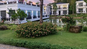 Un hôtel à la façade blanche, doté d’un espace extérieur aménagé et couvert, ainsi que d’un bassin dont l’eau reflète l’environnement.