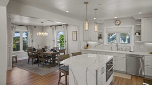 A modern kitchen with a marble island, wooden dining table, and pendant lighting. - Iaorana: Newly remodeled luxury 3 bedroom with Ocean Views (Carmel)