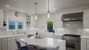 A modern kitchen with white cabinetry, a central island, stainless steel appliances, pendant lighting, and a clock on the wall. - Iaorana: Newly remodeled luxury 3 bedroom with Ocean Views (Carmel)