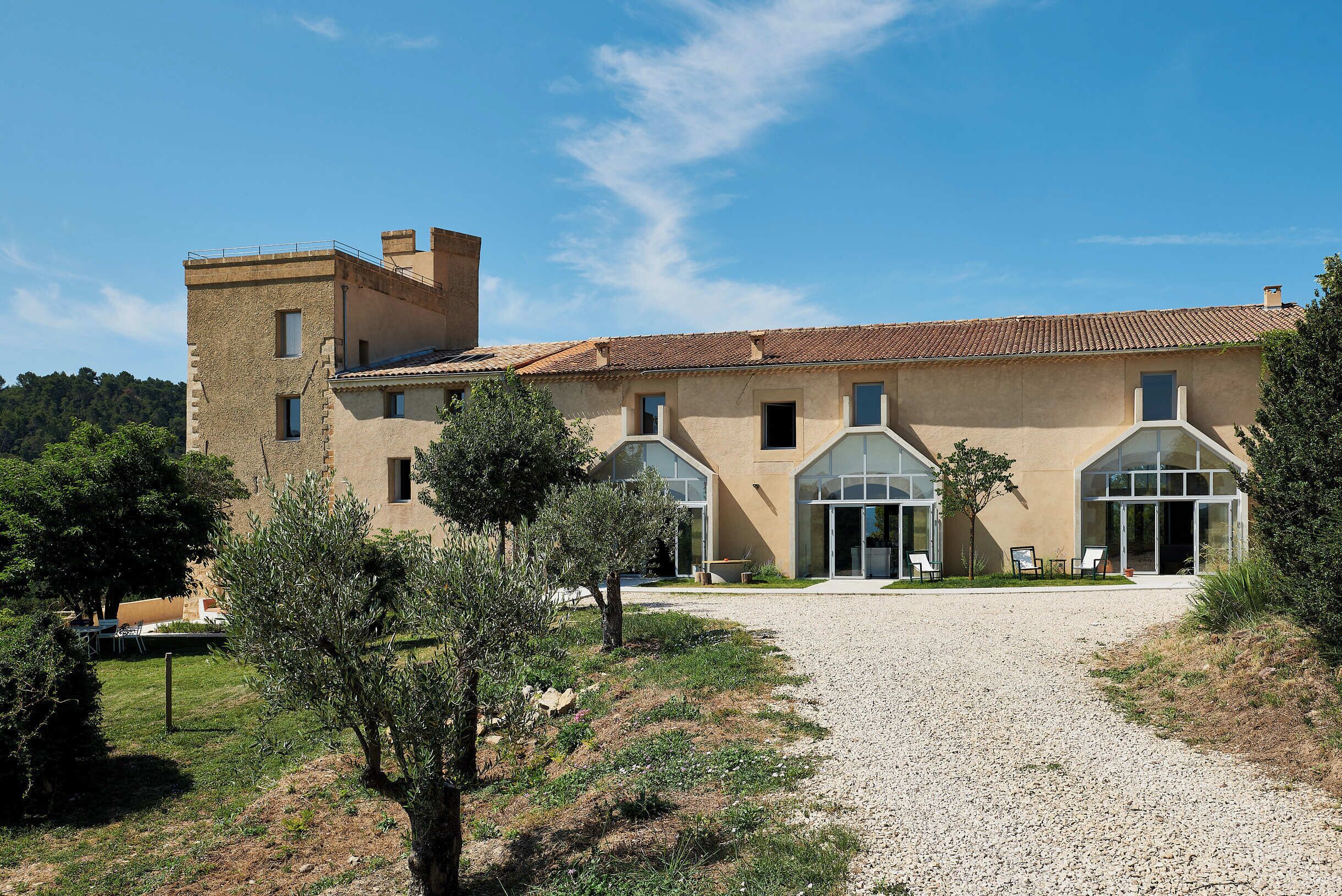 A building with a gravel driveway, a tree-lined path, and a clear blue sky.