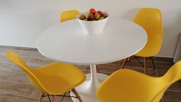 Een ronde witte tafel met een fruitschaal, omringd door vier gele stoelen.