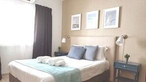 A neatly made bed with a white and blue bedspread, a teal throw blanket, and rolled towels. There are three framed pictures on the wall above the bed. - Coastal Escape with Backyard Beach, Inema INES (Lagos)